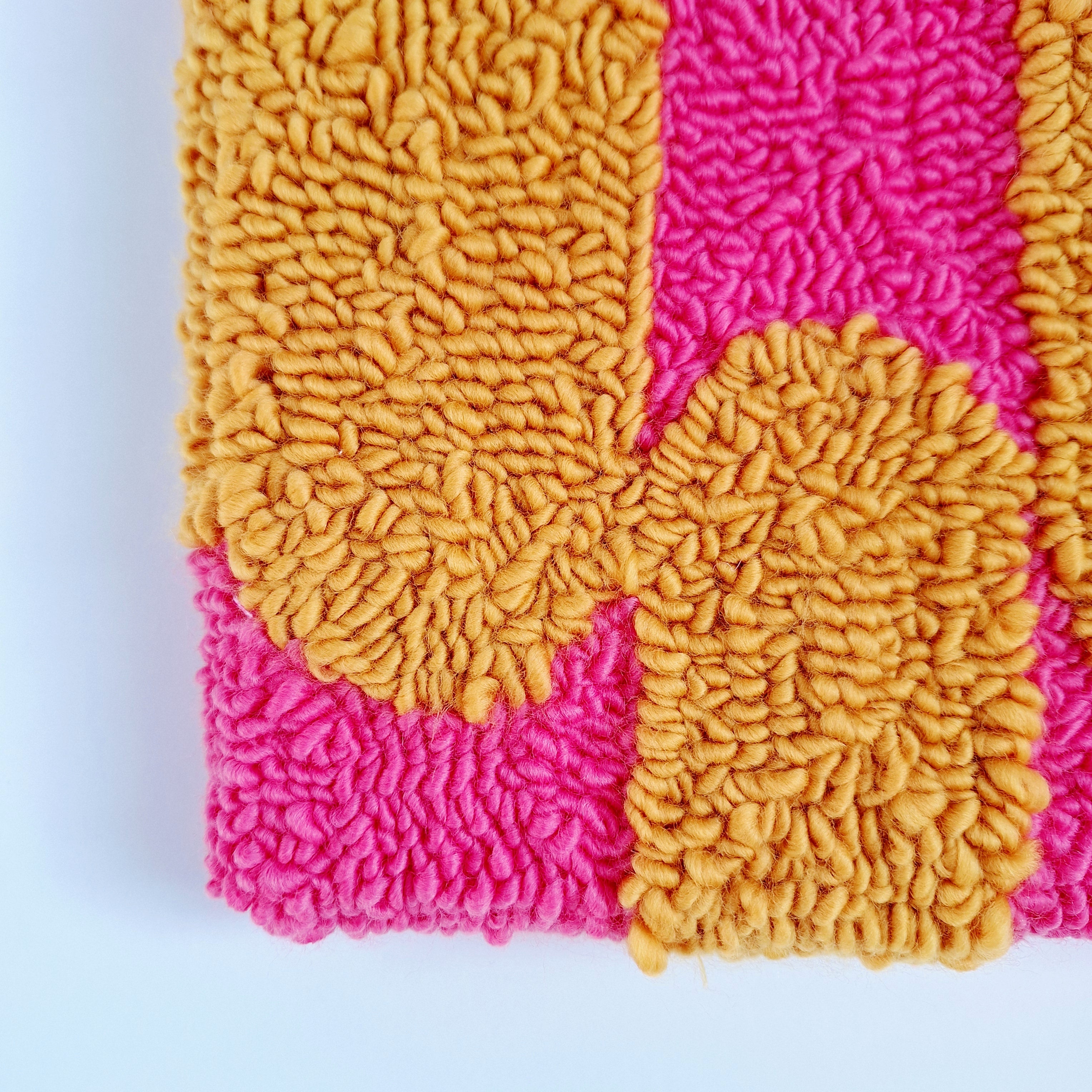 Vista de cerca de cuadro de lana realizado artesanalmente en punch needle. Color rosa y mostaza.
