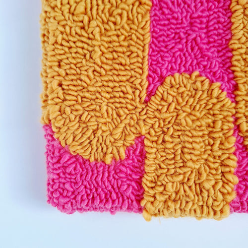 Vista de cerca de cuadro de lana realizado artesanalmente en punch needle. Color rosa y mostaza.