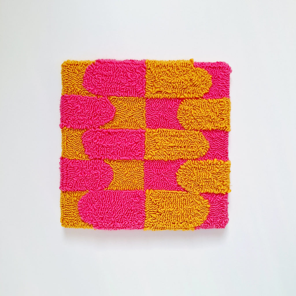 Vista frontal de cuadro de lana realizado artesanalmente en punch needle. Color rosa y mostaza.