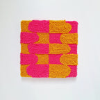Vista frontal de cuadro de lana realizado artesanalmente en punch needle. Color rosa y mostaza.