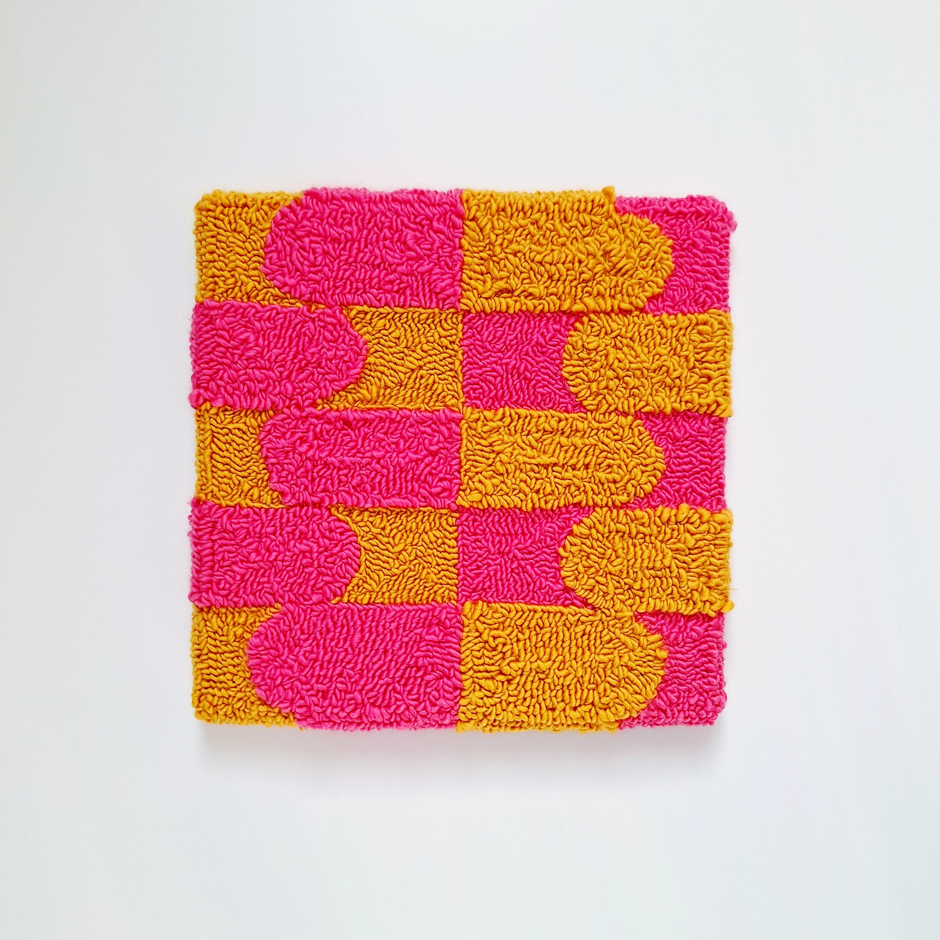 Vista frontal de cuadro de lana realizado artesanalmente en punch needle. Color rosa y mostaza.